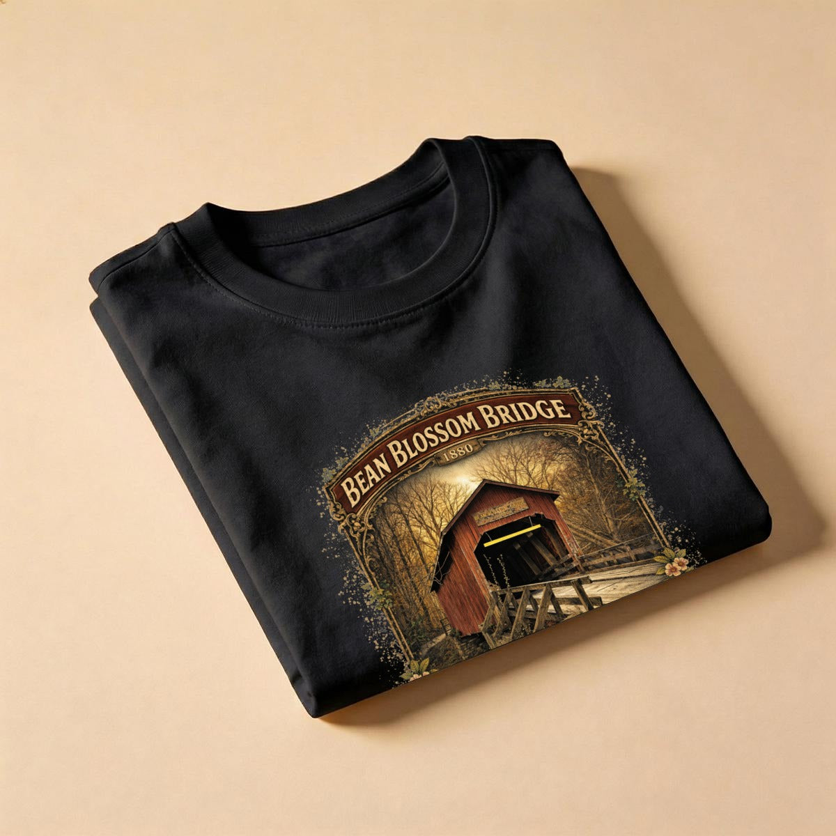 Folded Black t-shirt with graphic design - bean blossom bridge shirt on a beige background.
