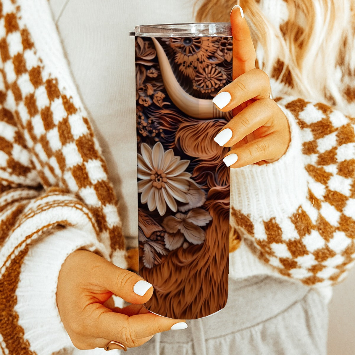 Person holding a20 oz straight tumbler with 3D tooled leather highlander cow design with a cozy indoor background.
