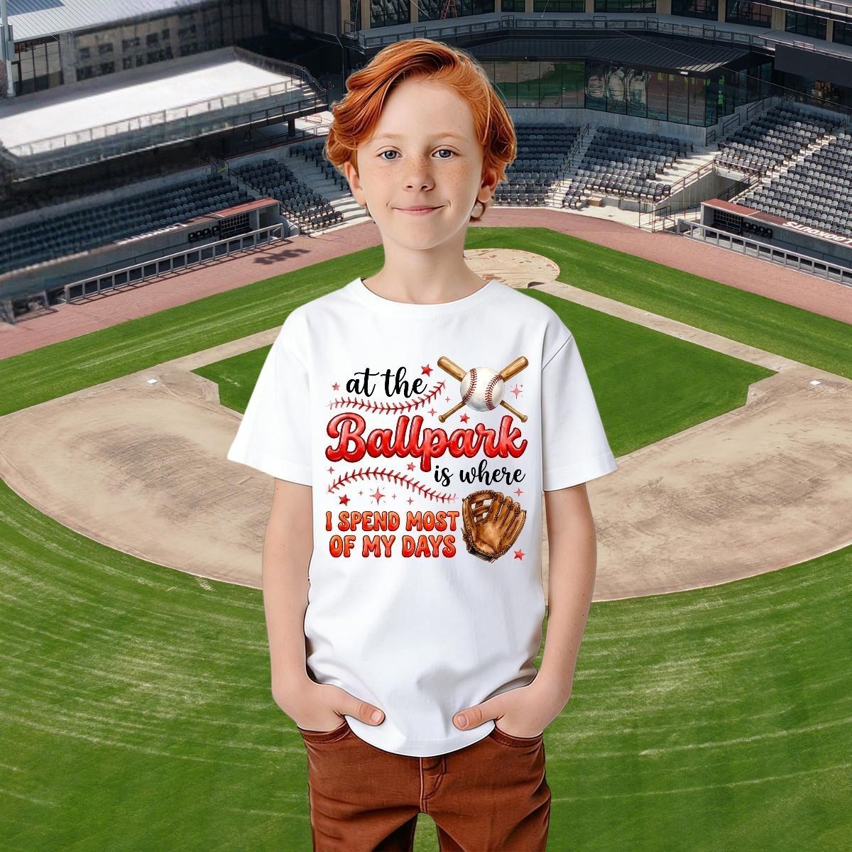 Child wearing a white t-shirt with a baseball-themed design on a baseball field background.