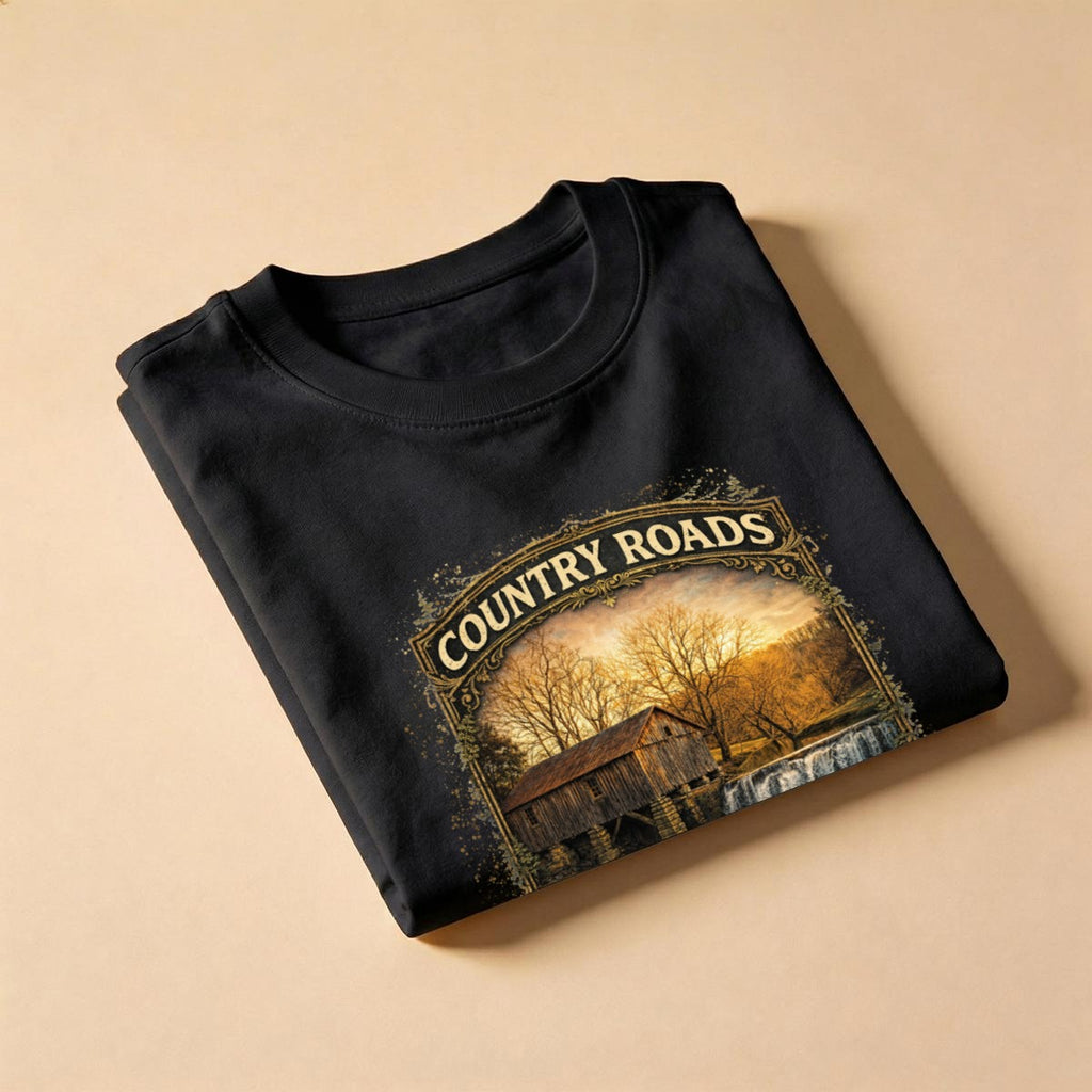 Folded Black t-shirt with graphic design - Country Roads-Take Me Home Shirt on a beige background.