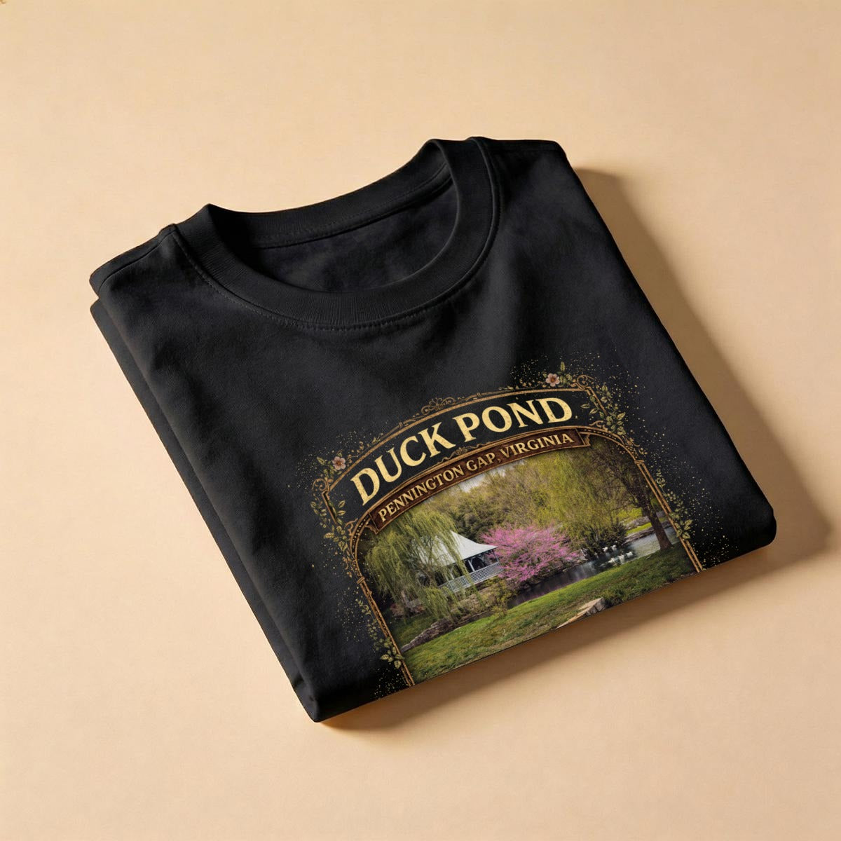 Folded black t-shirt with Duck Pond graphic design on a beige background.