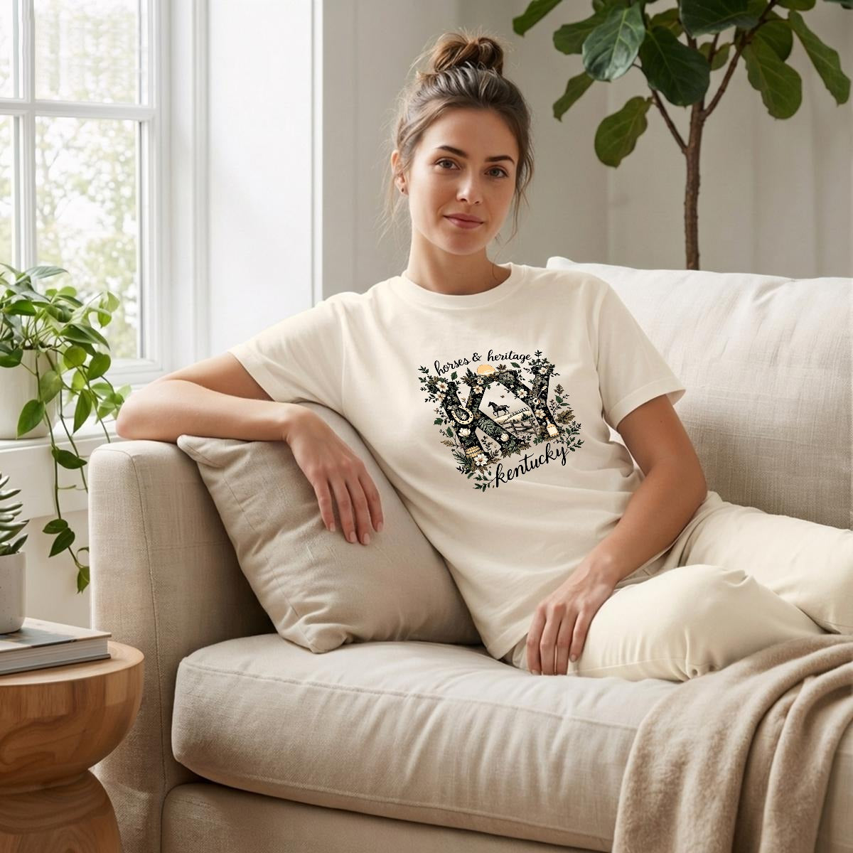 Woman sitting on a couch wearing a natural-colored t-shirt with a colorful graphic design.