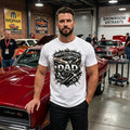 Man wearing a Master of Repairs Dad t-shirt standing next to a red car in a garage.