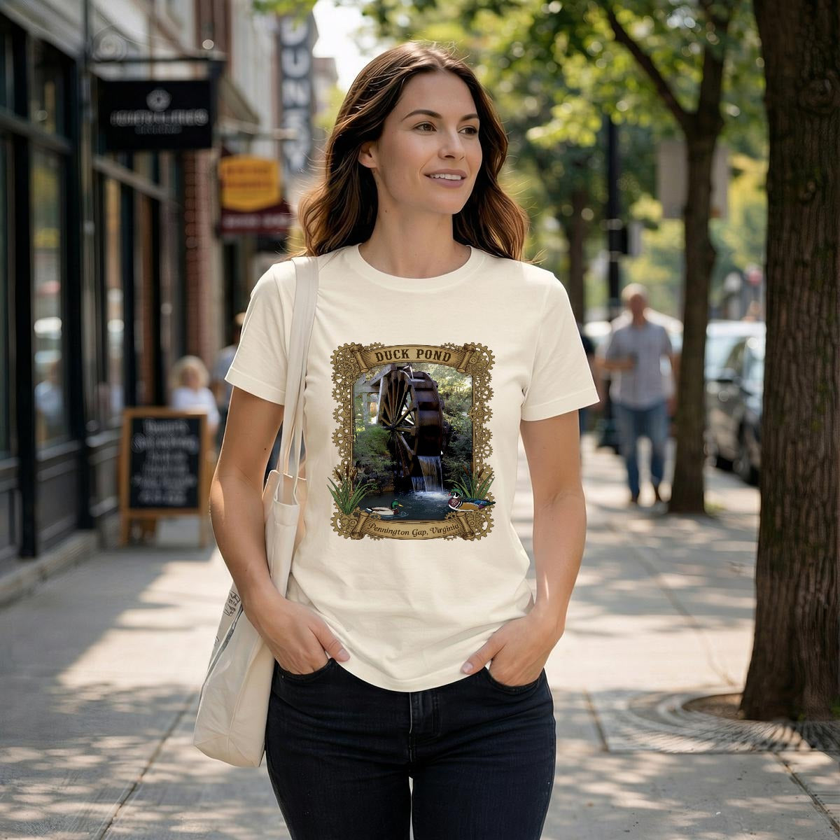 Woman wearing a cream-colored tee with a rustic watermill, graphic with text duck pond Pennington Gap, VA.