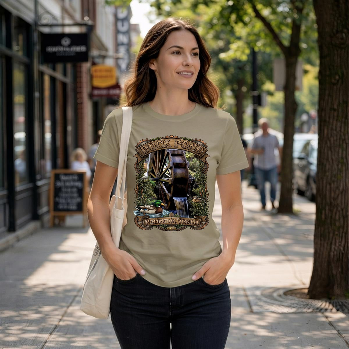 Woman wearing a tan tee with a rustic watermill, graphic with text duck pond Pennington, Gap VA.
