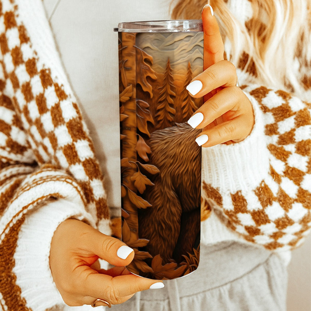 Person holding a20 oz straight tumbler with 3D tooled leather grizzly bear design with a cozy indoor background.