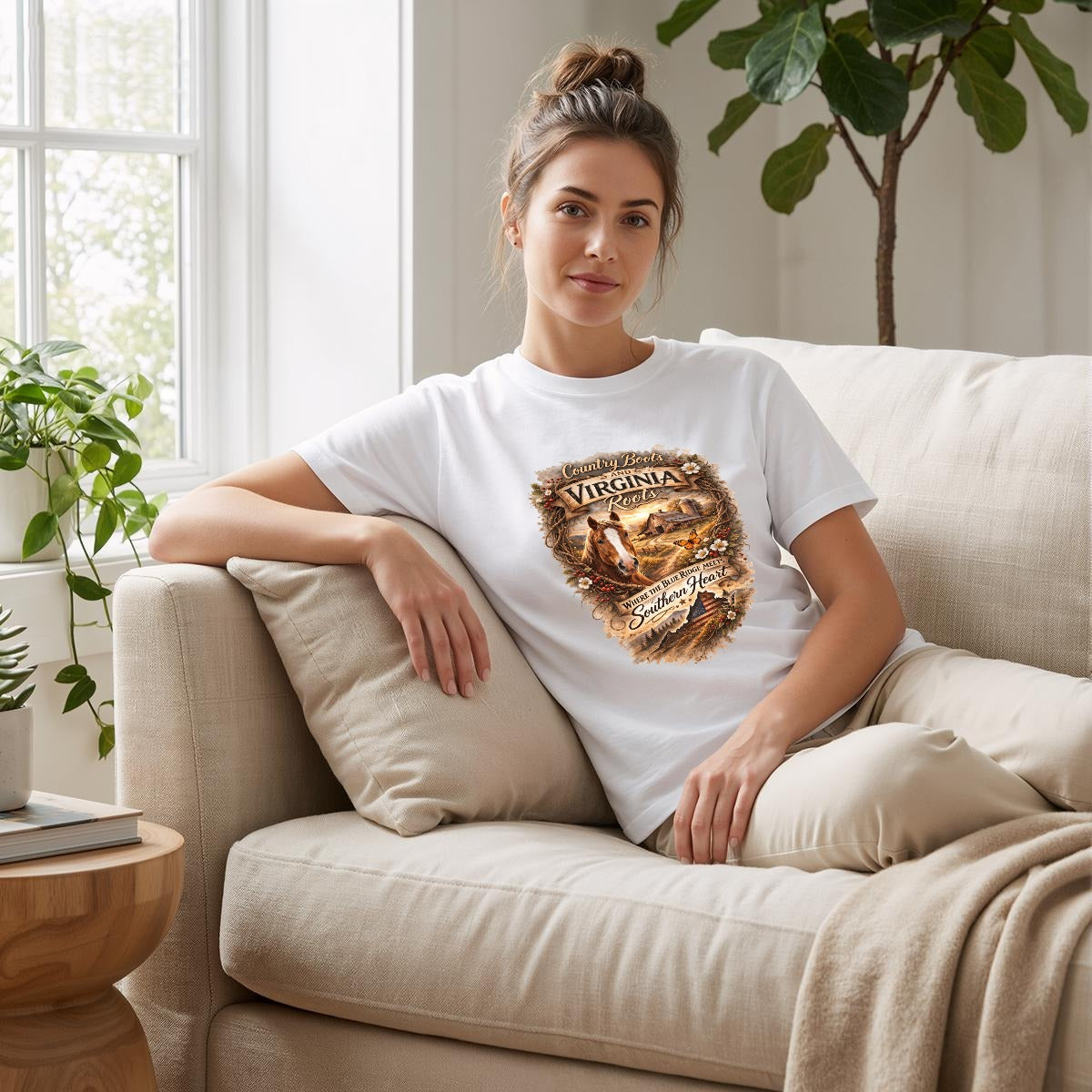 Woman sitting on a couch wearing a white t-shirt with graphic and text - Virginia Roots and Southern Heart Country.